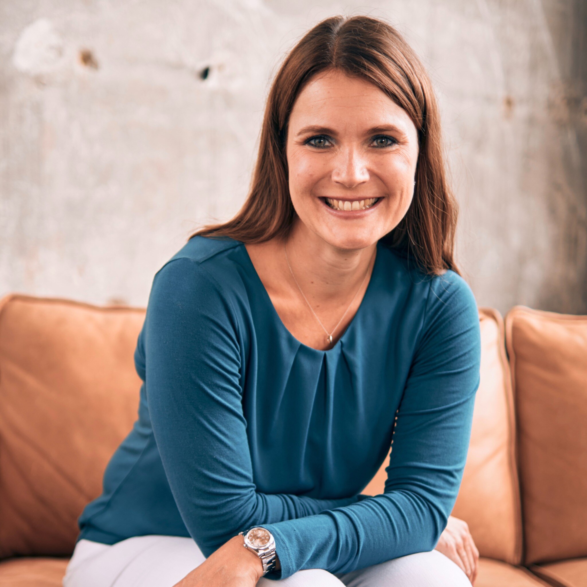 Vanessa Butz sitzt lächelnd auf einem Ledersofa.